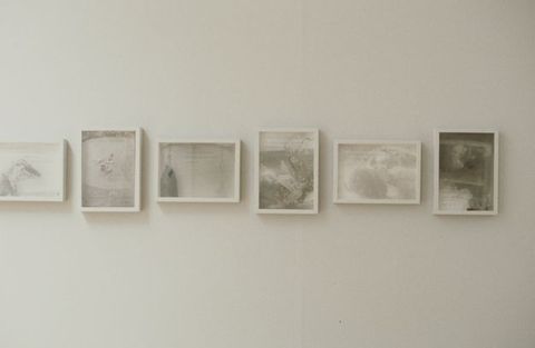 Installation photograph. Six white-framed photographs are printed with silvery, vaporous tones of grey to capture misty, nearly abstract shapes and forms. The photographs alternate between vertical and horizontal orientation.